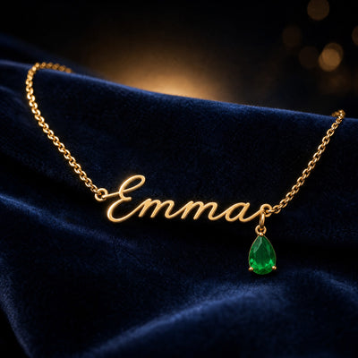 Gold name necklace in cursive script with an emerald teardrop birthstone